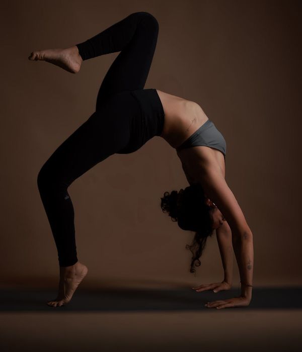 Woman in a balanced yoga pose against a dark background with teal accents.